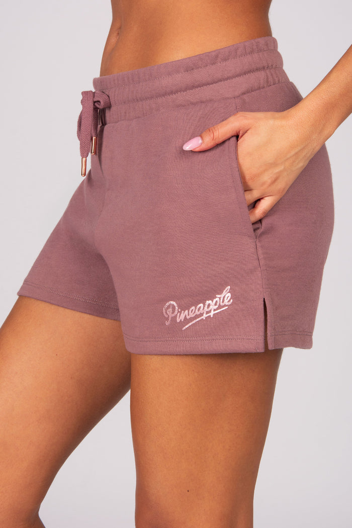 Light brown shorts with 'Pineapple' logo and pockets worn by a woman on a light grey background
