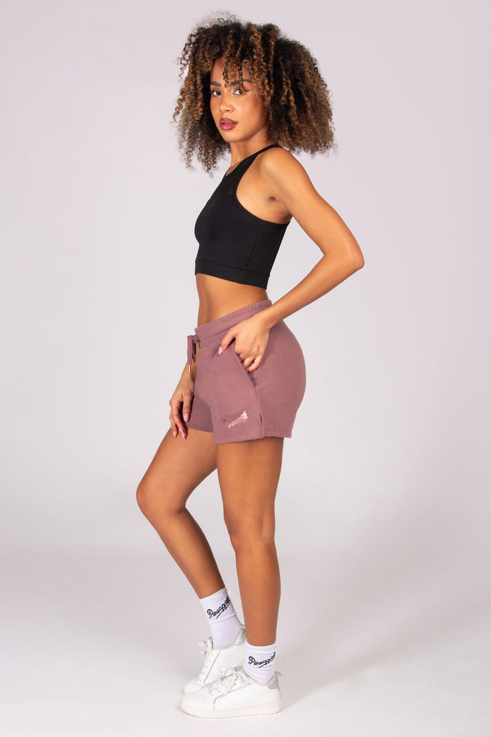 Woman wearing a black sports bra and light brown sporty shorts on a white background
