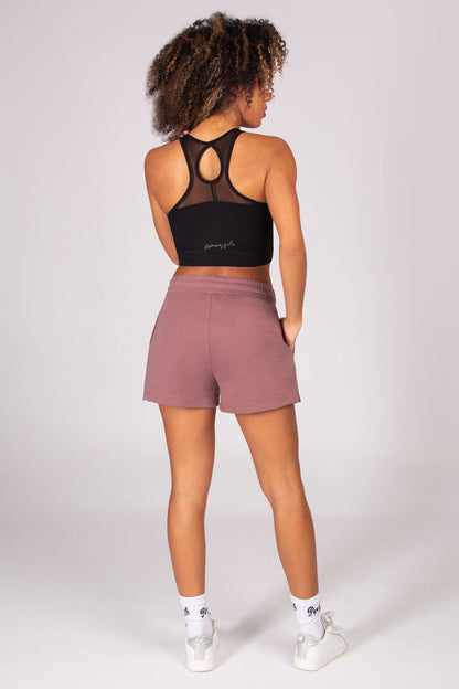 Woman wearing a black sports bra and sporty light brown shorts on a white background