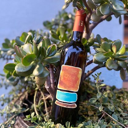 Dark wine bottle with red-orange foil cap and colorful rectangular label panels