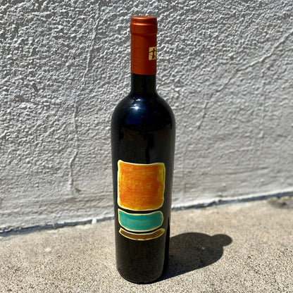 Dark wine bottle with red-orange foil cap and colorful rectangular label