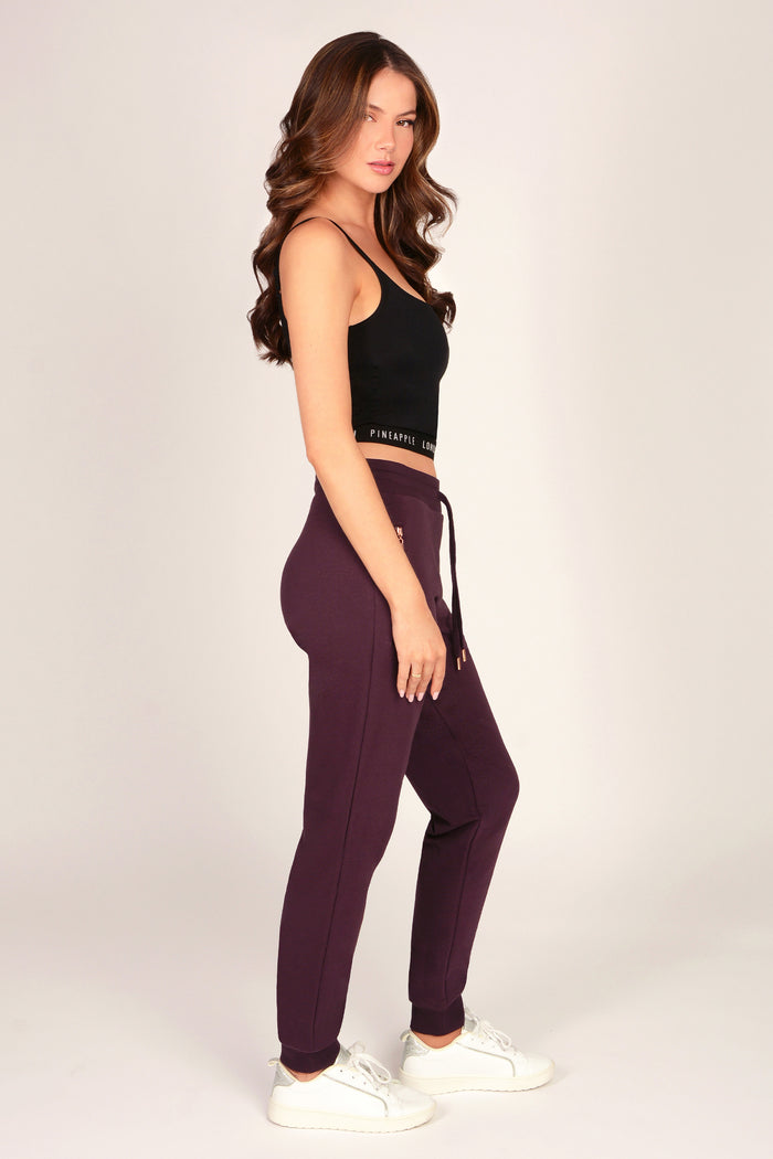 Woman wearing slim fit joggers with zip pockets and drawcord waistband paired with black tank top on a plain background.