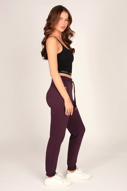 Woman wearing slim fit joggers with zip pockets and drawcord waistband paired with black tank top on a plain background.
