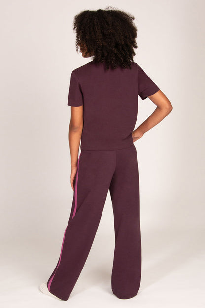 Girl wearing maroon brown trousers with pink side panel and matching t-shirt on a plain background