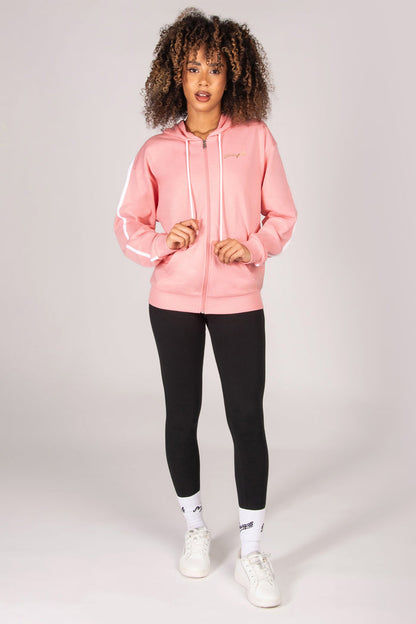 Woman wearing a light pink zip hoodie, black leggings, and white sneakers on a light grey background