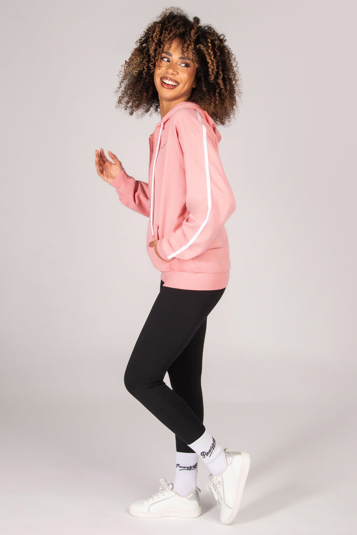 Woman wearing a light pink hoodie, black leggings, and white sneakers on a light grey background