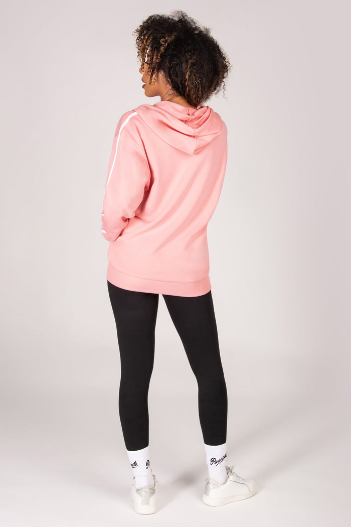 Woman wearing a light pink hoodie and black leggings on a white background