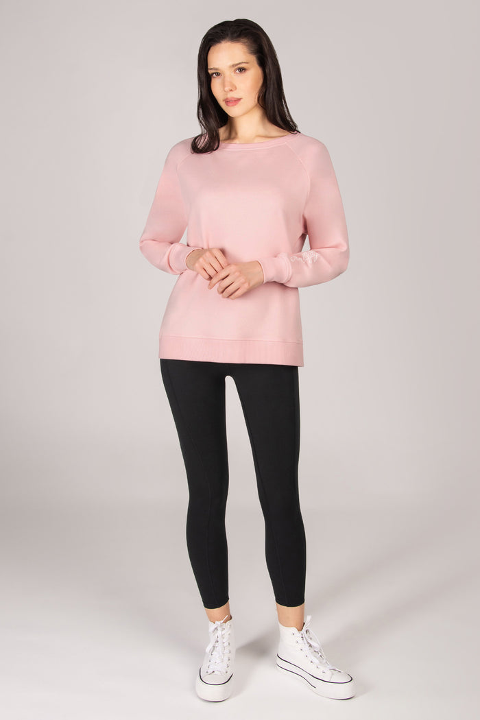 Woman wearing a light pink sweatshirt with black leggings against a plain background