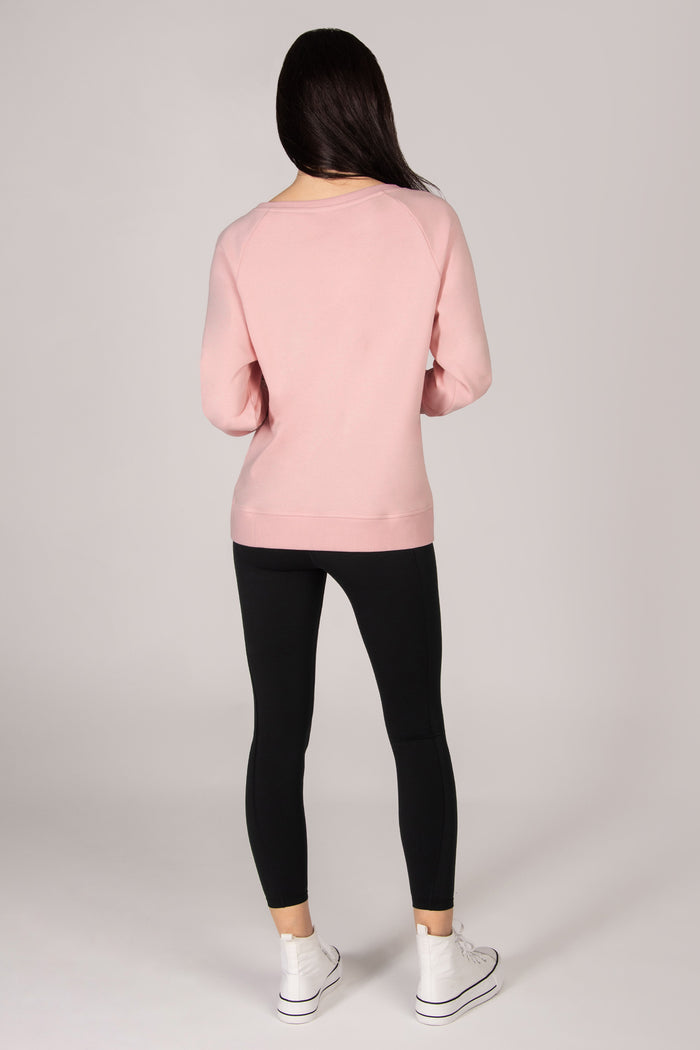 Woman wearing a pink sweatshirt with black leggings on a grey backdrop