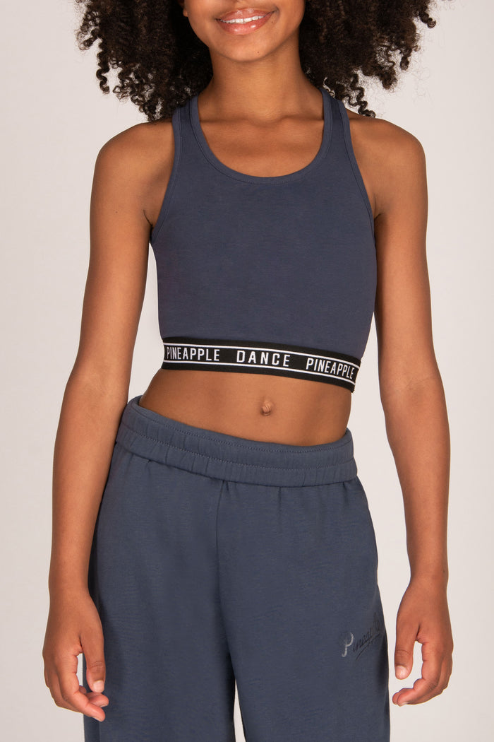 A model wearing a dark grey athletic crop top with a black and white 'PINEAPPLE DANCE' branded waistband, paired with matching oversized sweatpants, against a grey background.