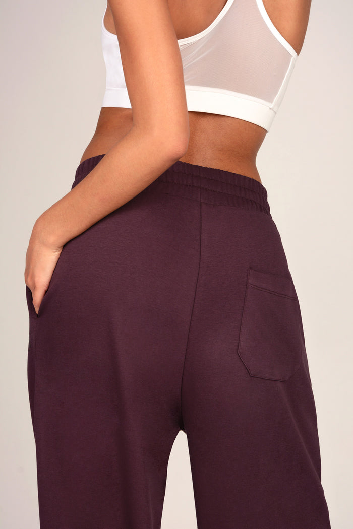 Close up shot of a pair of dark aubergine joggers from the back, featuring a back pocket.