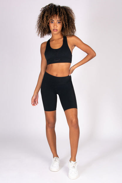 Woman wearing a black super soft sports bra and cycling shorts set on a white background