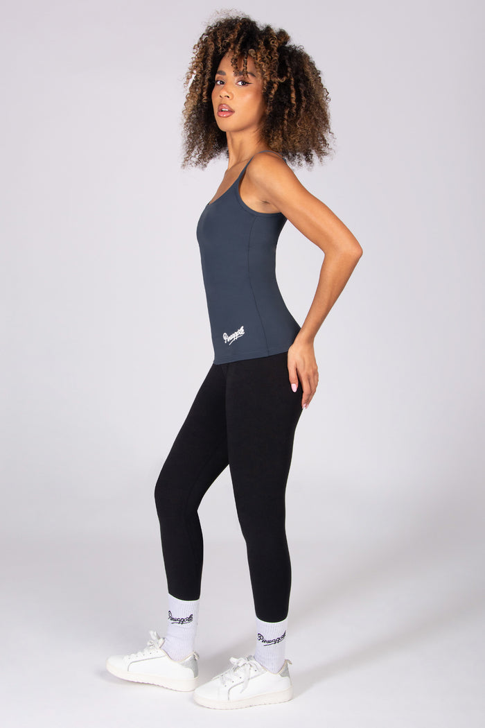 Woman wearing a dark grey tank top with adjustable straps and black leggings on a plain background