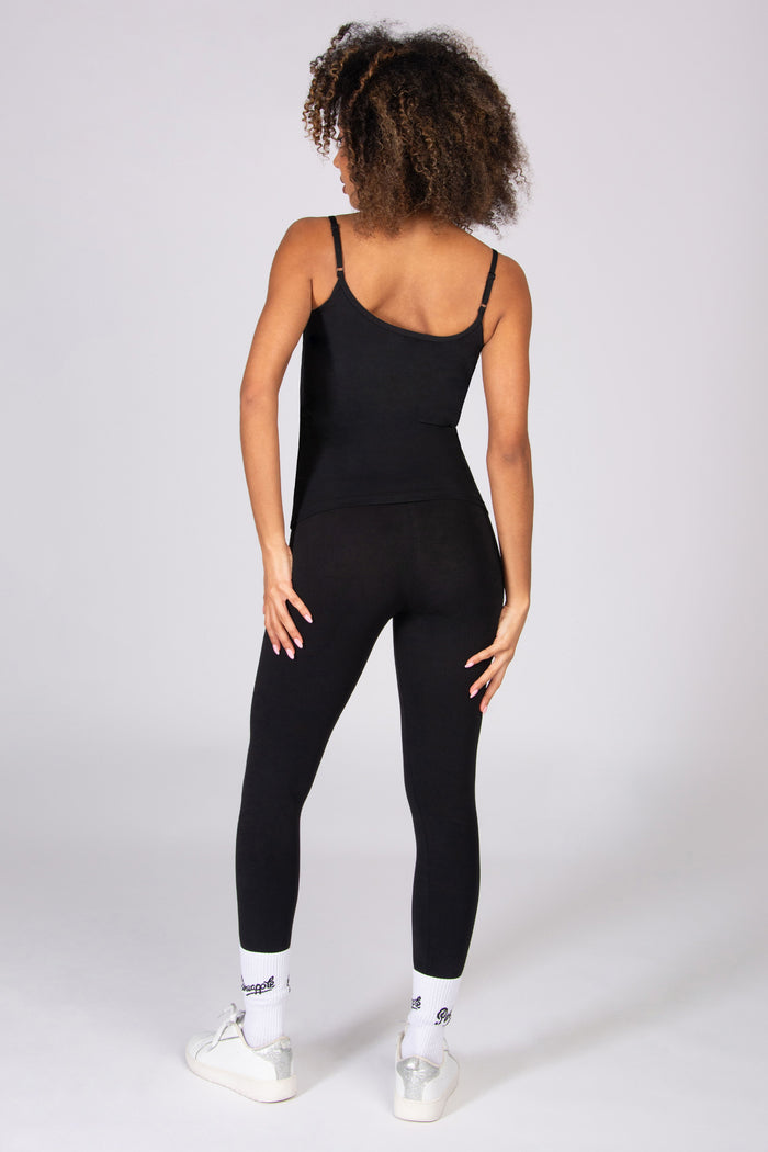 Woman wearing a black tank top with adjustable straps and black leggings on a white background