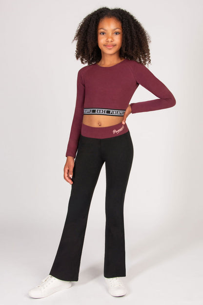 Girl wearing a burgundy long-sleeve crop top and black flares on a white background