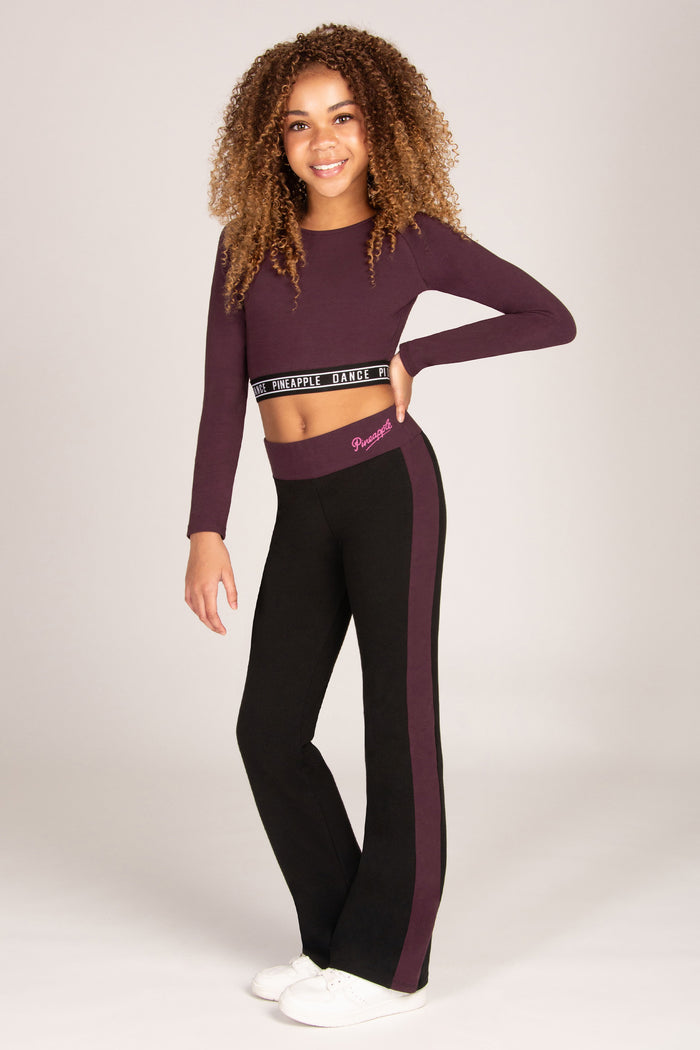 Girl wearing a maroon brown long-sleeve crop top and matching black flared trousers on a plain background