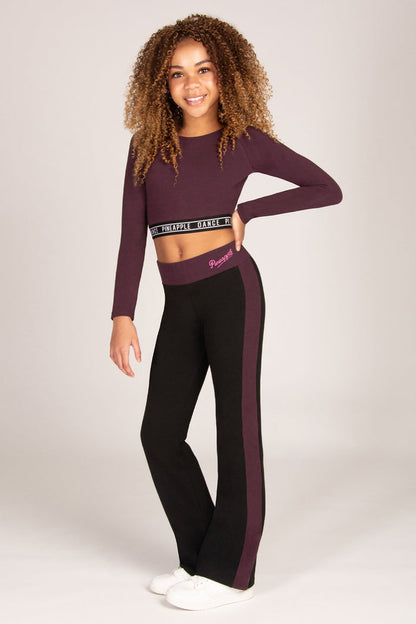 Girl wearing a maroon brown long-sleeve crop top and matching black flared trousers on a plain background