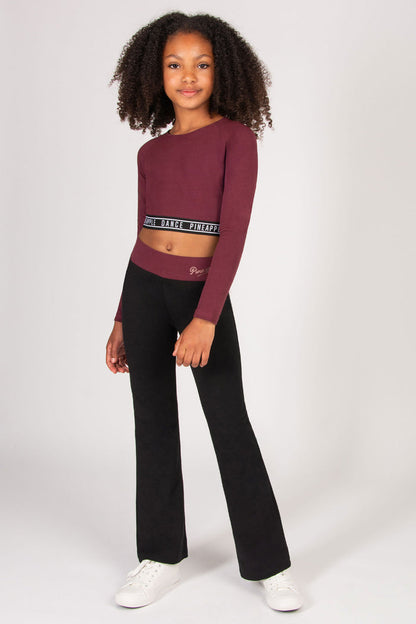 Young girl wearing a burgundy long-sleeve crop top and black flared trousers on a white background
