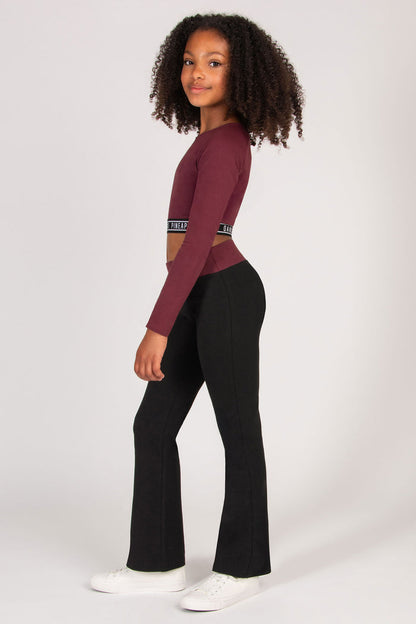 Girl wearing a burgundy long-sleeve crop top and black pants on a white background