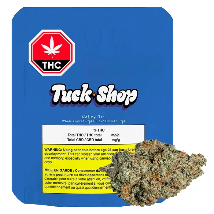 Front-facing shot of the Tuck Shop Valley Girl 7 g package on blue backing with a cannabis bud overlapping the lower right.