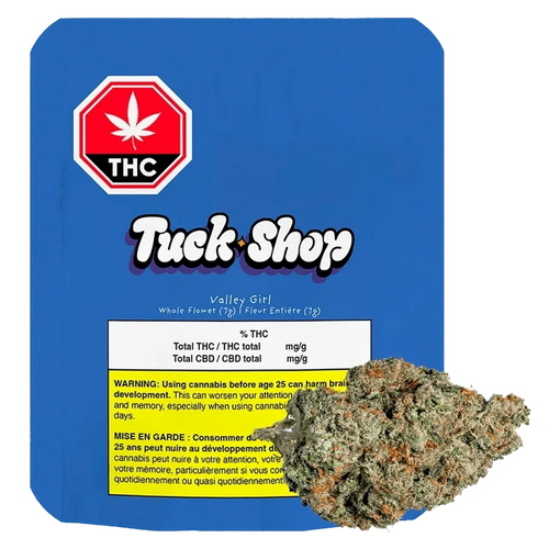 Front-facing shot of the Tuck Shop Valley Girl 7 g package on blue backing with a cannabis bud overlapping the lower right.
