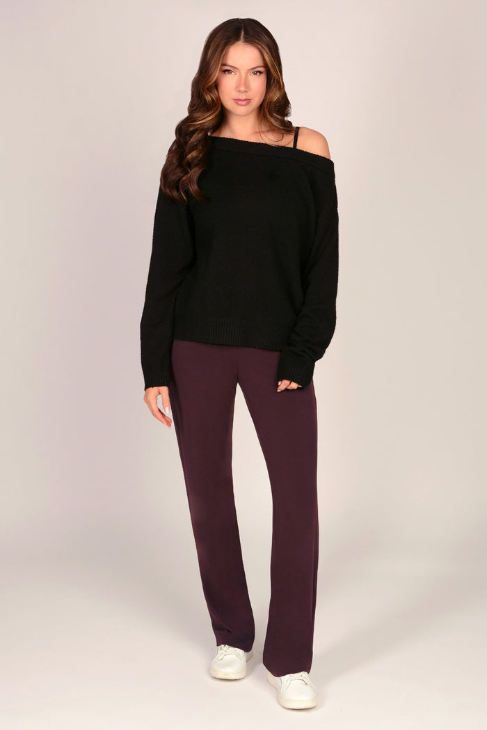 Woman wearing a black off-shoulder sweater and maroon brown viscose trousers on a plain background