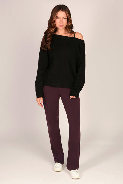 Woman wearing a black off-shoulder sweater and maroon brown viscose trousers on a plain background