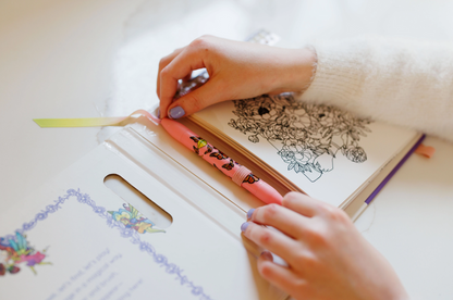 Person coloring in a coloring book with markers on a white surface