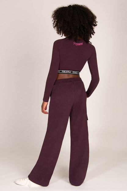 Girl wearing a maroon brown wide-leg trousers with pockets and matching long-sleeve top on a white background