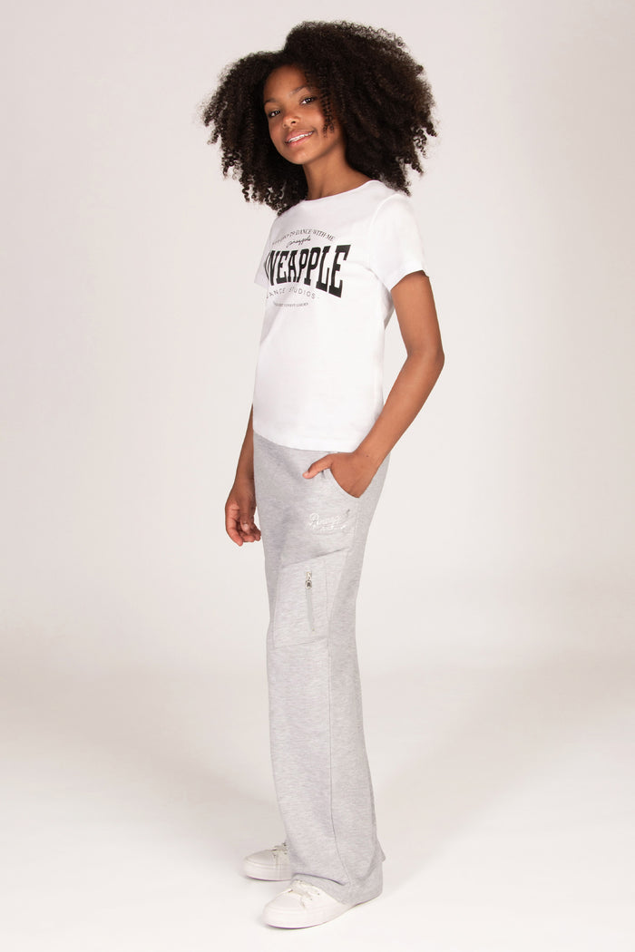 A young girl wearing a white short-sleeve graphic t-shirt and light grey marl trousers with cargo pockets.